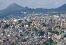 Vista de comunidade urbana com moradias densas em área montanhosa, ilustrando problemas de moradia no Brasil e crescimento desordenado.