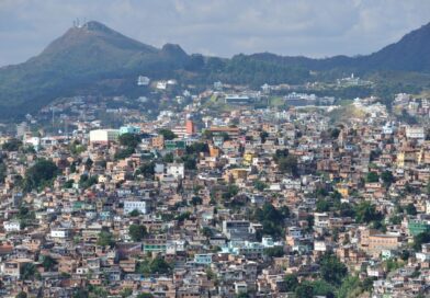 Vista de comunidade urbana com moradias densas em área montanhosa, ilustrando problemas de moradia no Brasil e crescimento desordenado.