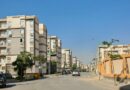 Conjunto de prédios residenciais em área urbana, com rua tranquila, carros estacionados e infraestrutura típica de moradia em condomínio.